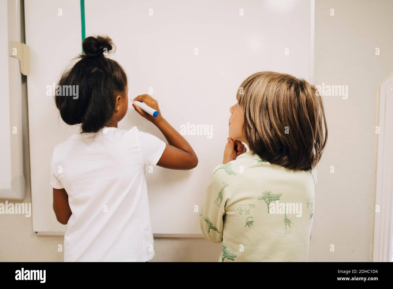 Ragazzo che guarda la studentessa che scrive sulla lavagna nella scuola elementare Foto Stock