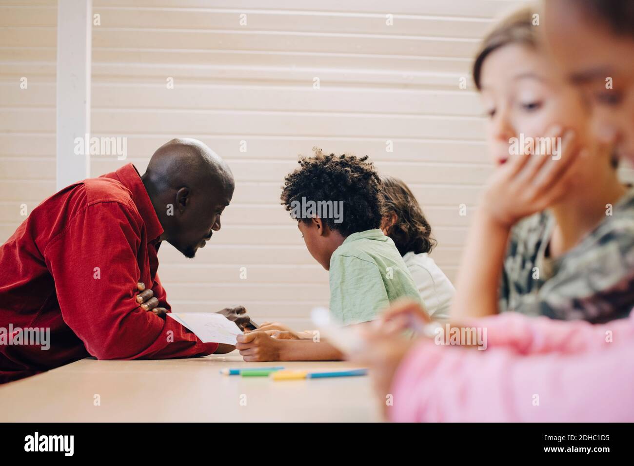 Insegnante che guida gli studenti nell'apprendimento tramite il tablet digitale alla scrivania in classe Foto Stock