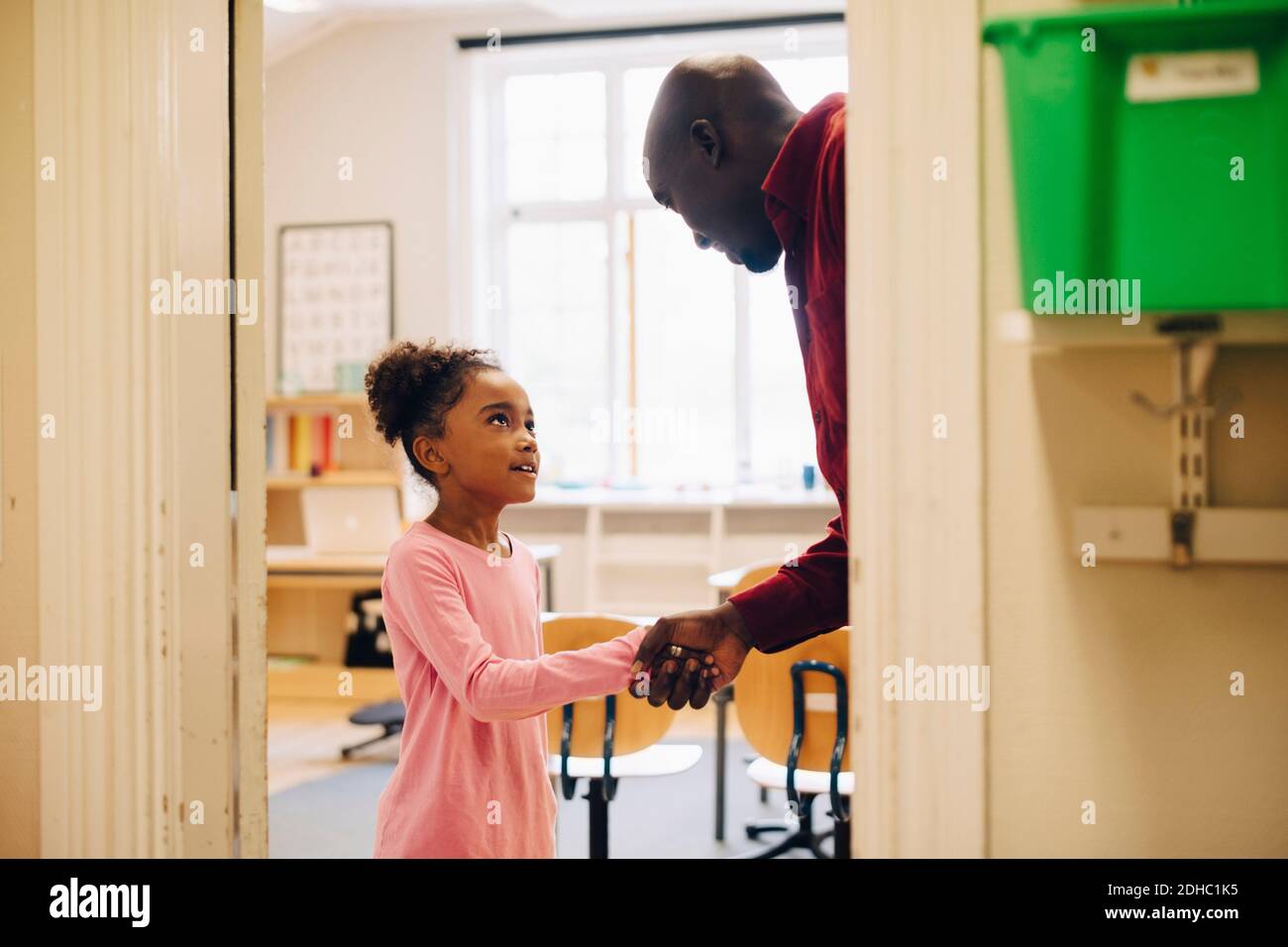 Insegnante che scuote la mano con il ragazzo alla porta in classe Foto Stock