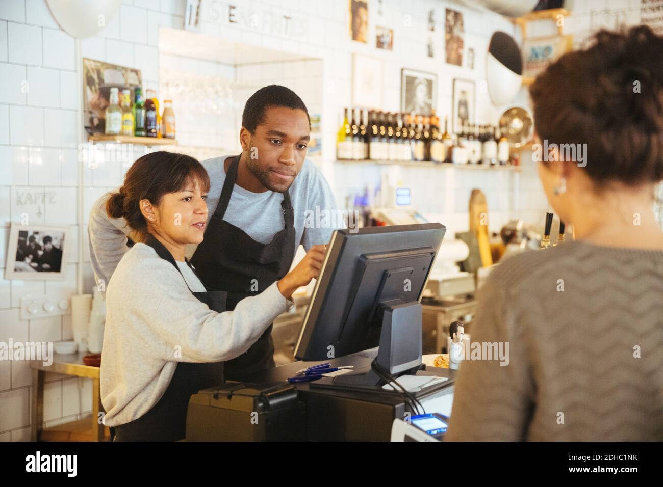 Giovane dipendente in piedi da cassiere femminile utilizzando il computer con il cliente al banco del check-out in delicatessen Foto Stock