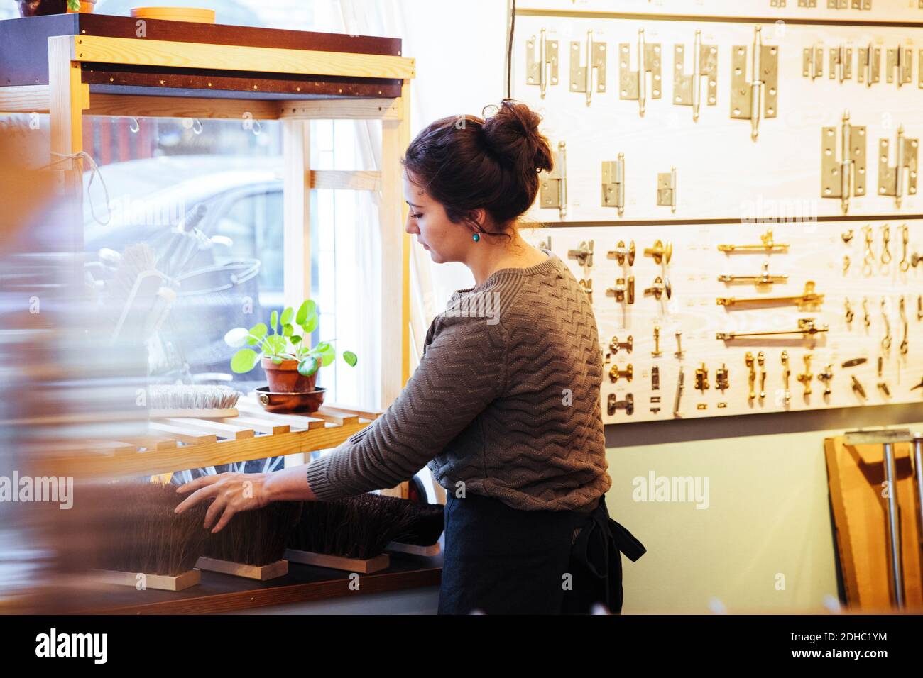 Giovane donna proprietario che posiziona scopa su rack a casa miglioramento negozio Foto Stock