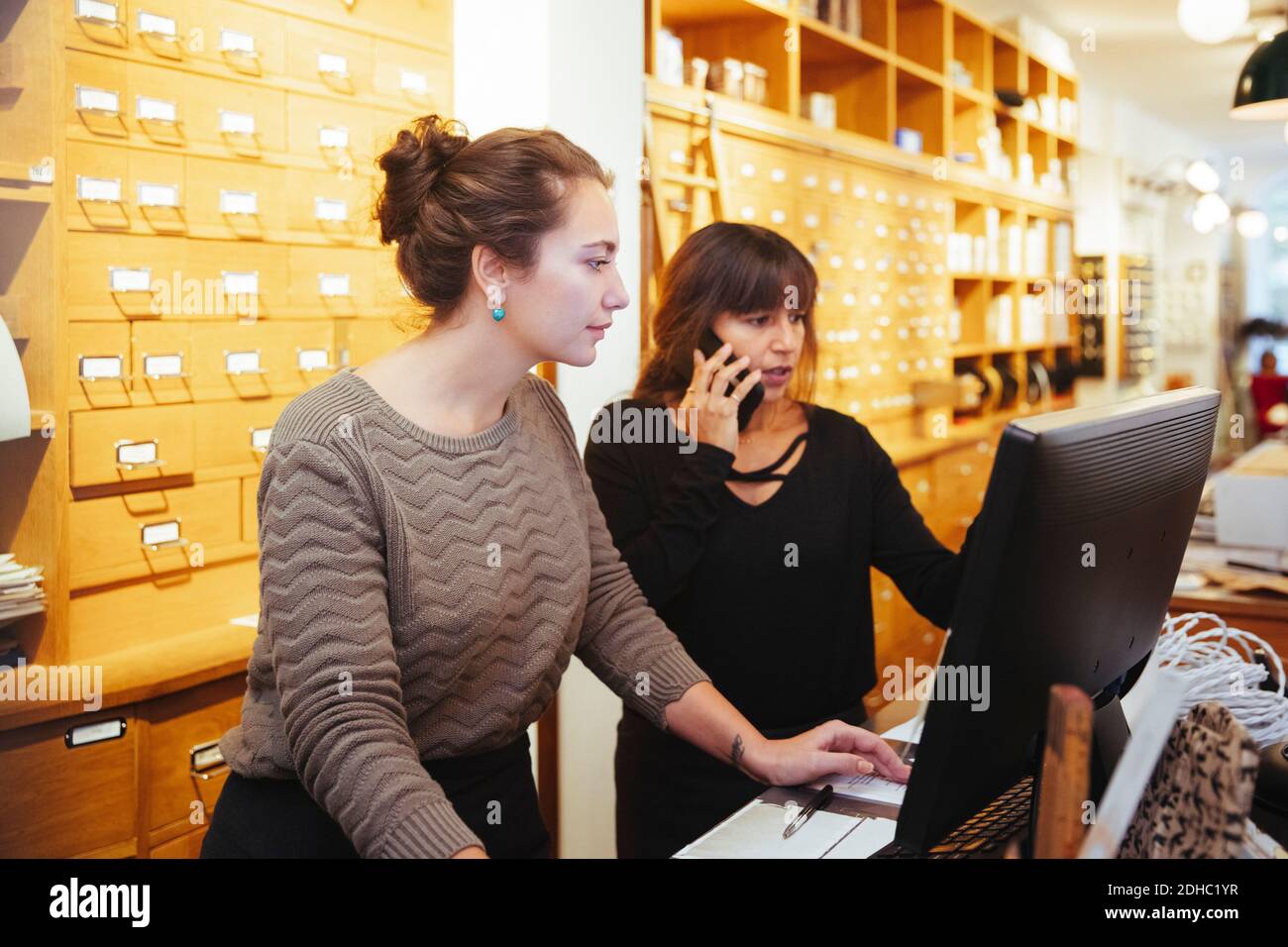 Donna matura che parla su smartphone in piedi per le vendite impiegato che usa il computer al momento del check-out nel negozio di mobili Foto Stock