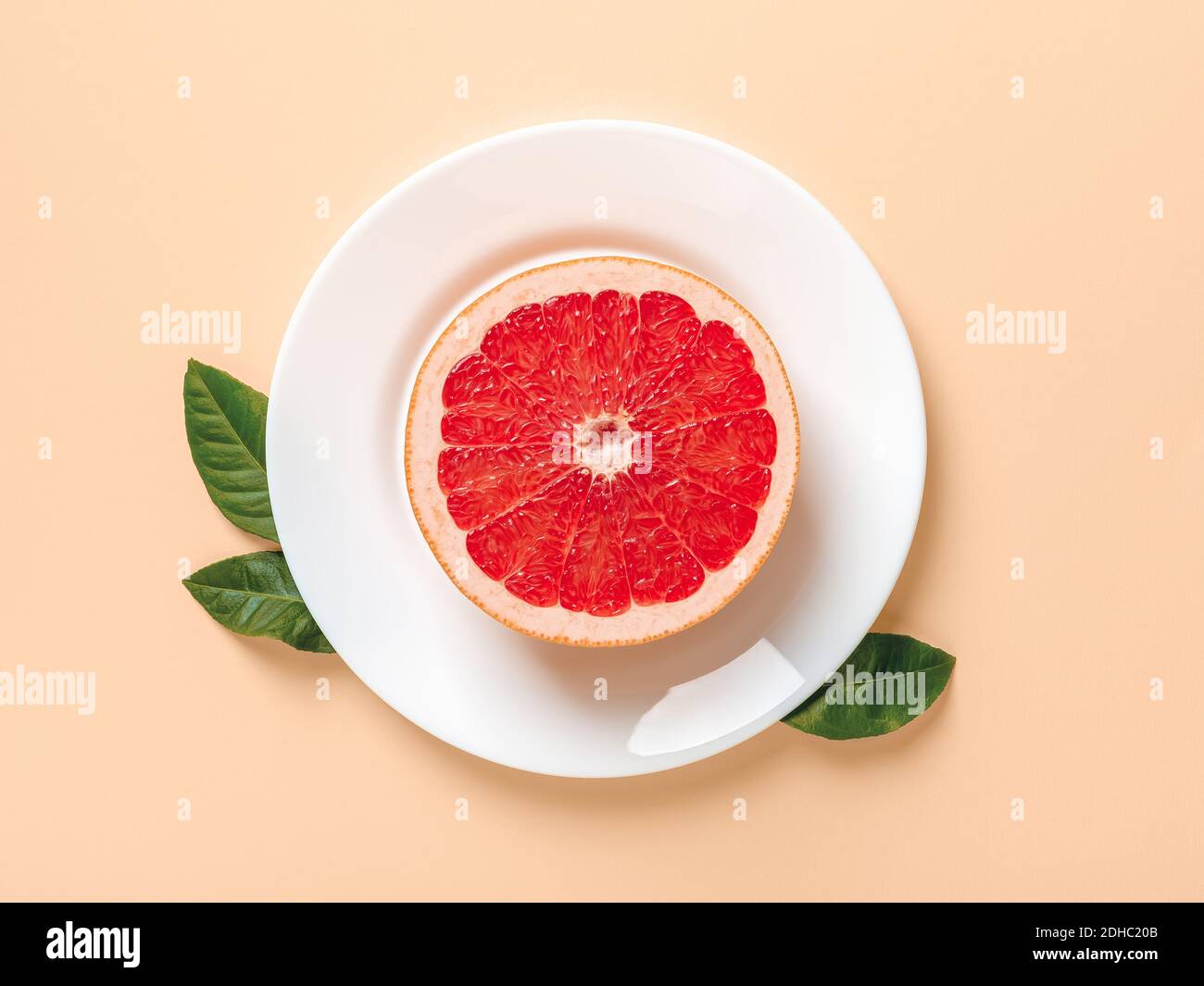 Metà di pompelmo succoso maturo su un piatto bianco e poche foglie verdi su sfondo beige. Dieta dimagrante, controllo del peso corporeo, alimentazione sana di vitamina Foto Stock