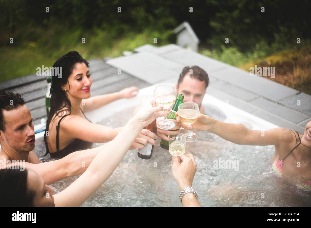 Spensierate amici maschi e femmine che tostano le bevande nella vasca idromassaggio durante la fuga del fine settimana Foto Stock