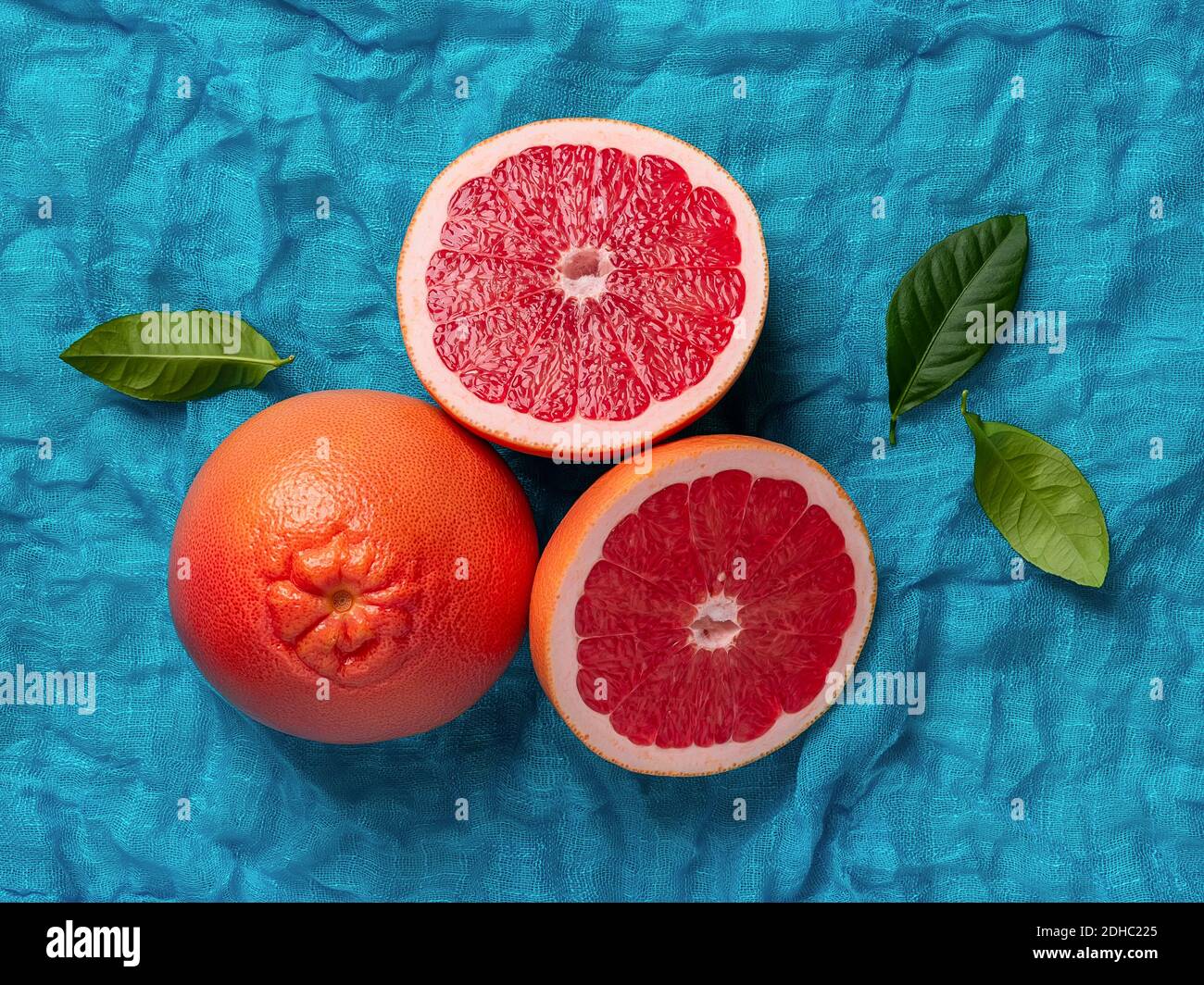 Pompelmo maturo intero e due succose metà su uno sfondo di tessuto turchese. Ingrediente per dolci di frutta. Cibo vegetariano gustoso e dieta dimagrante. Foto Stock