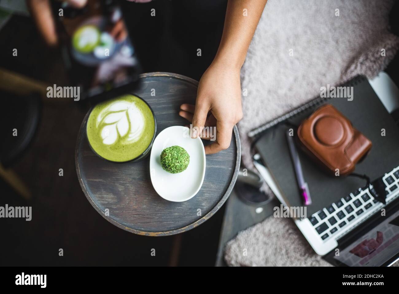 Direttamente sopra la vista di blogger femmina fotografando il tè matcha e. snack tramite smartphone in ufficio creativo Foto Stock