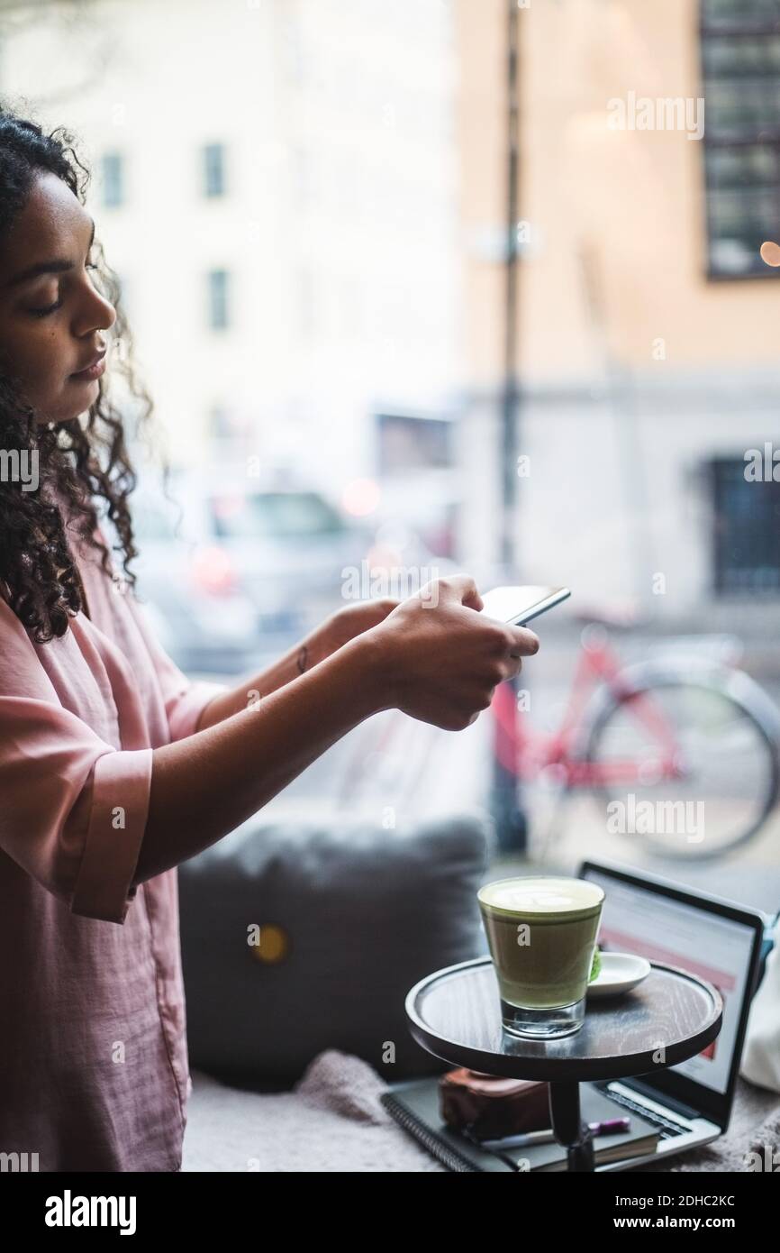Giovane blogger femmina fotografando tè e snack sul tavolo attraverso smartphone in ufficio creativo Foto Stock