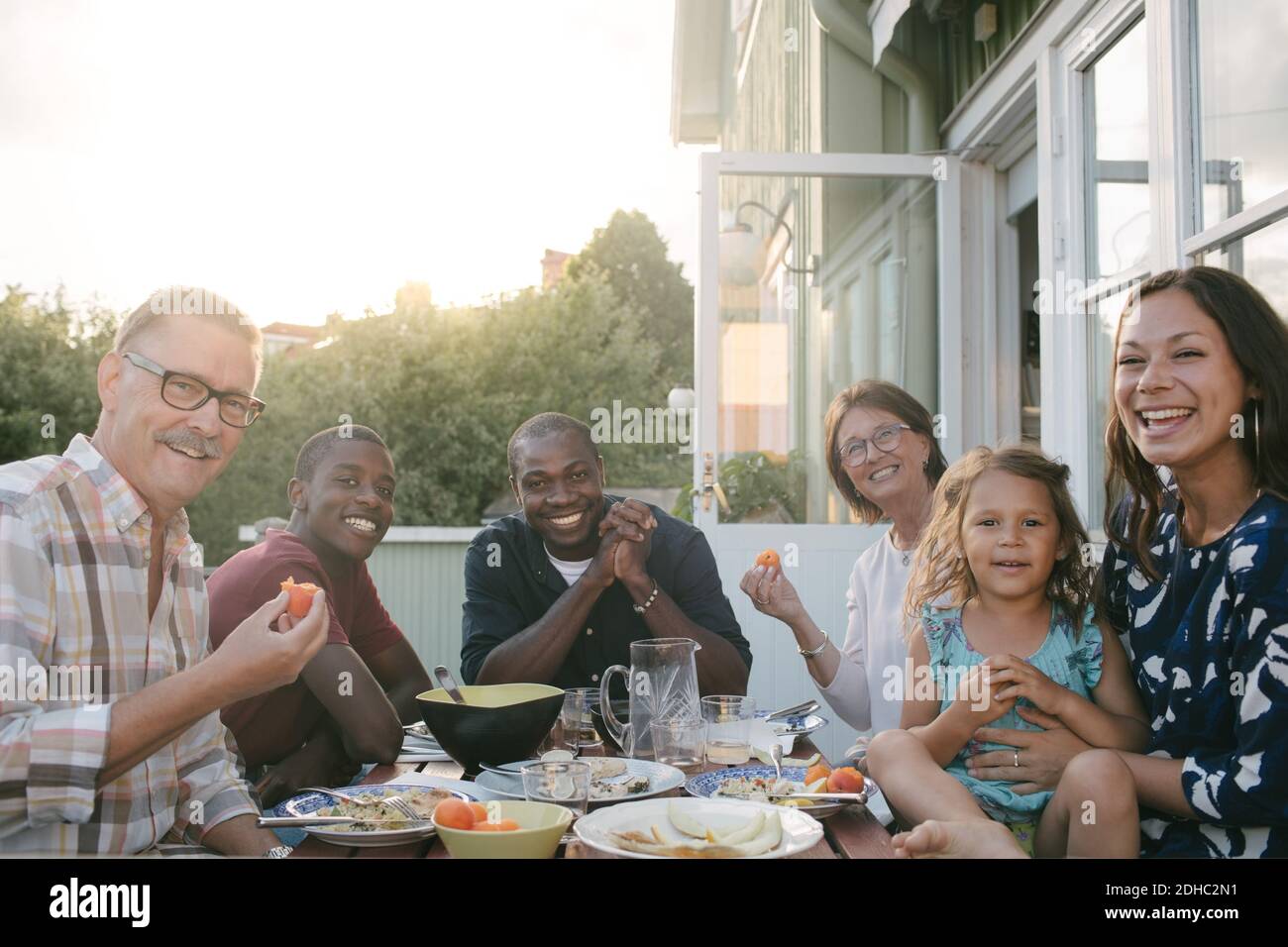 Ritratto di una famiglia sorridente e multigenerata che gusterai il pranzo al tavolo portico Foto Stock