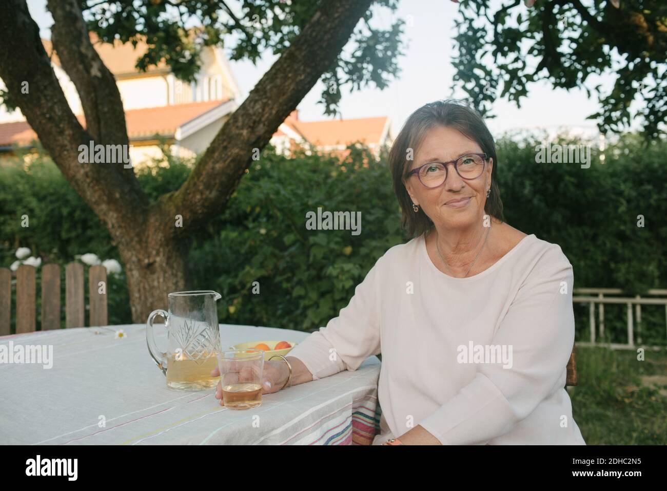Ritratto di donna sorridente che tiene un drink mentre si siede al tavolo in cortile Foto Stock