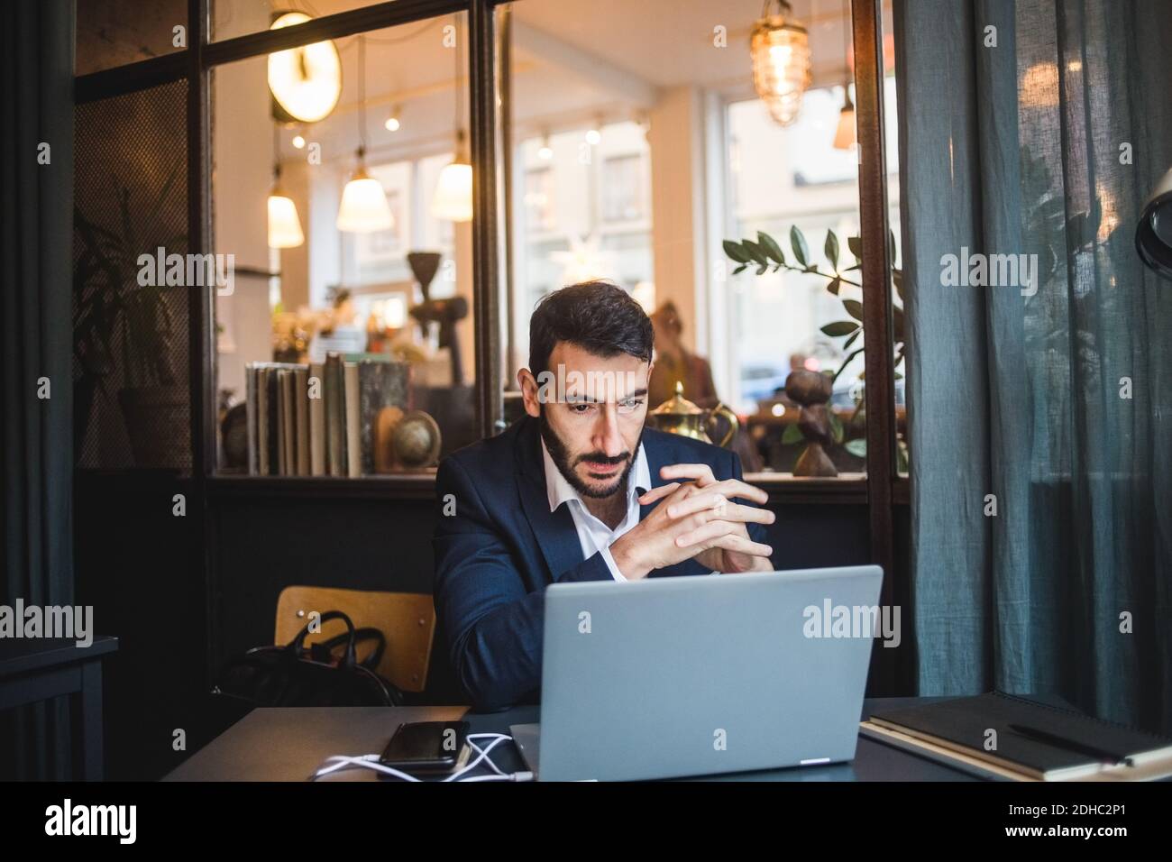 Uomo d'affari sicuro con le mani attaccate guardando il computer portatile sulla scrivania in ufficio creativo Foto Stock