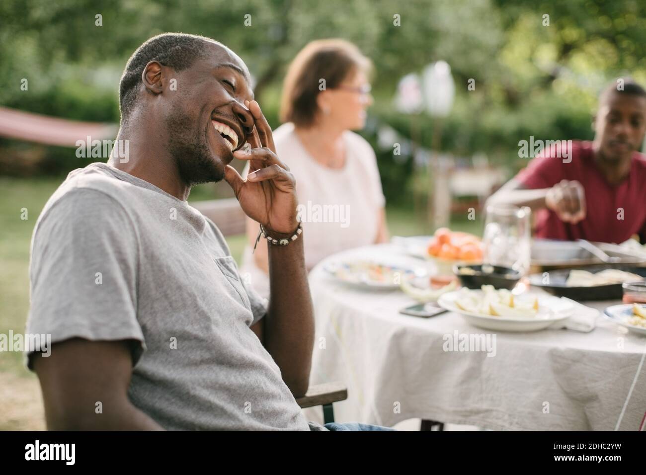 Uomo medio adulto sorridente mentre si siede al tavolo durante il giardino festa Foto Stock