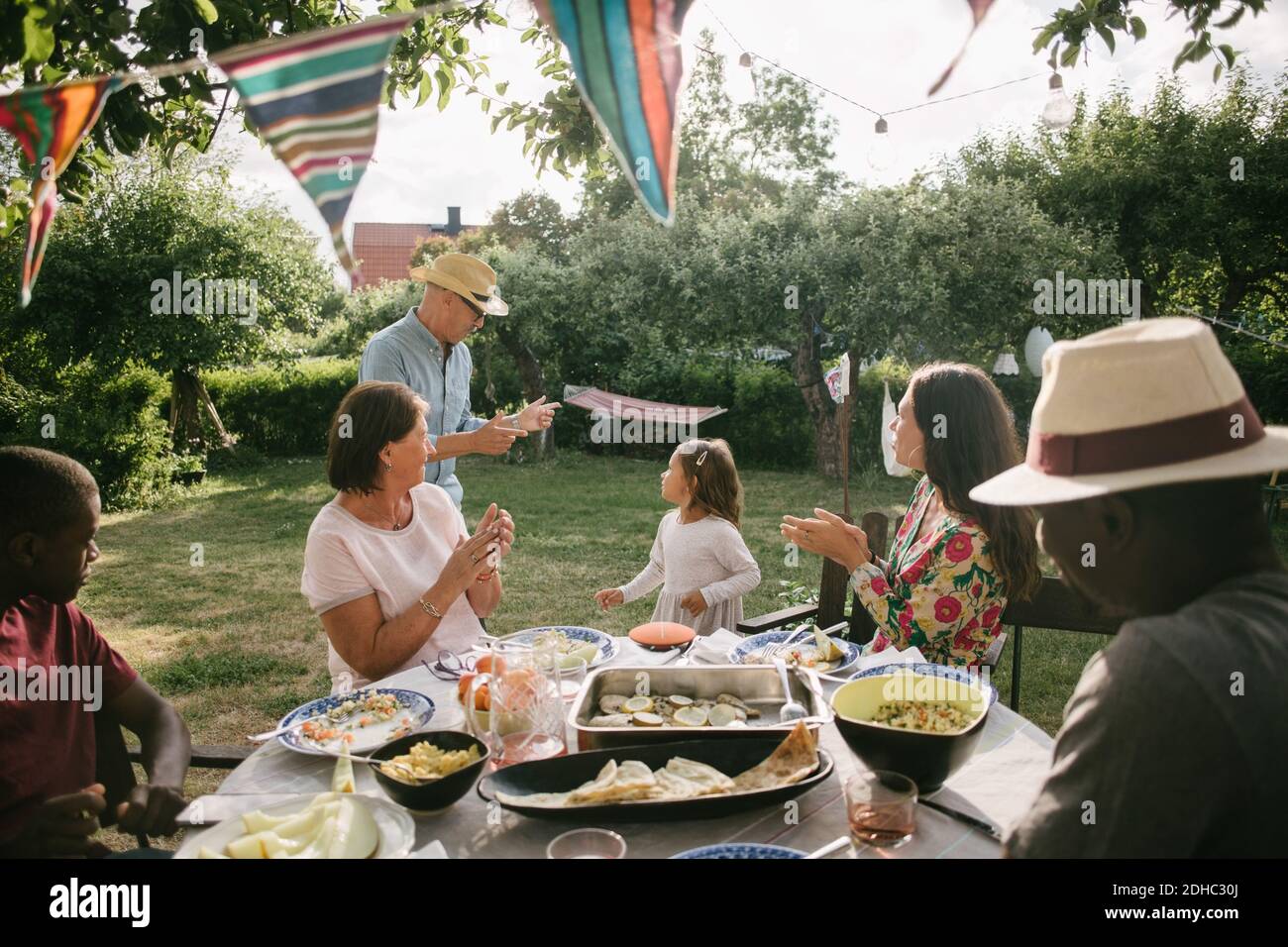 Famiglia applaudendo a uomo anziano e ragazza che danzano durante il giardino festa Foto Stock