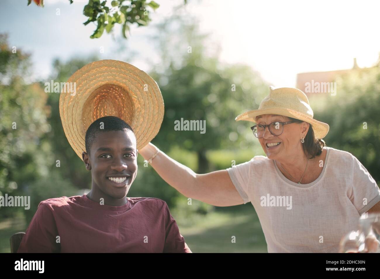 Nonna felice che tiene il cappello di paglia sopra il nipote durante la festa del giardino il giorno di sole Foto Stock