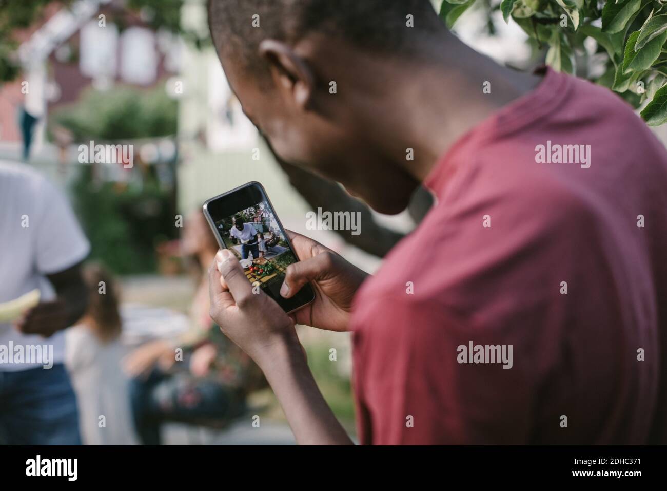 Ragazzo sorridente fotografando padre in cortile durante la festa in giardino Foto Stock