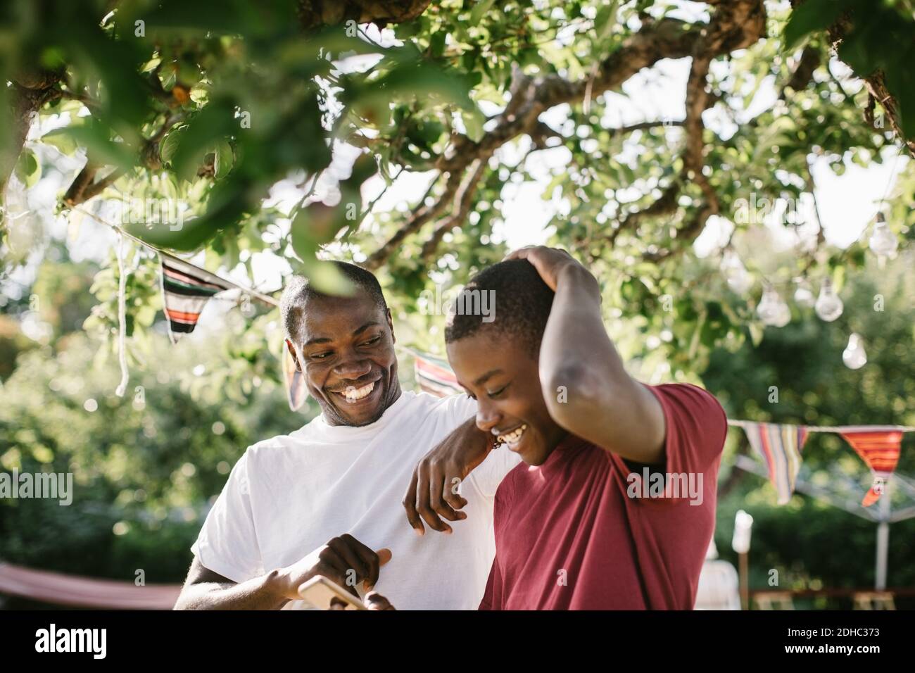 Felice padre che guarda il figlio usando il telefono mobile nel cortile durante la festa in giardino Foto Stock