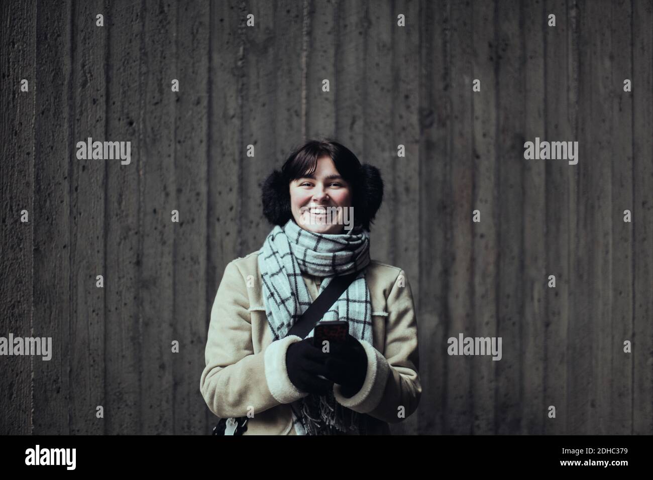 Ritratto di giovane donna allegra che indossa abiti caldi mentre si è in piedi contro il muro in metropolitana Foto Stock