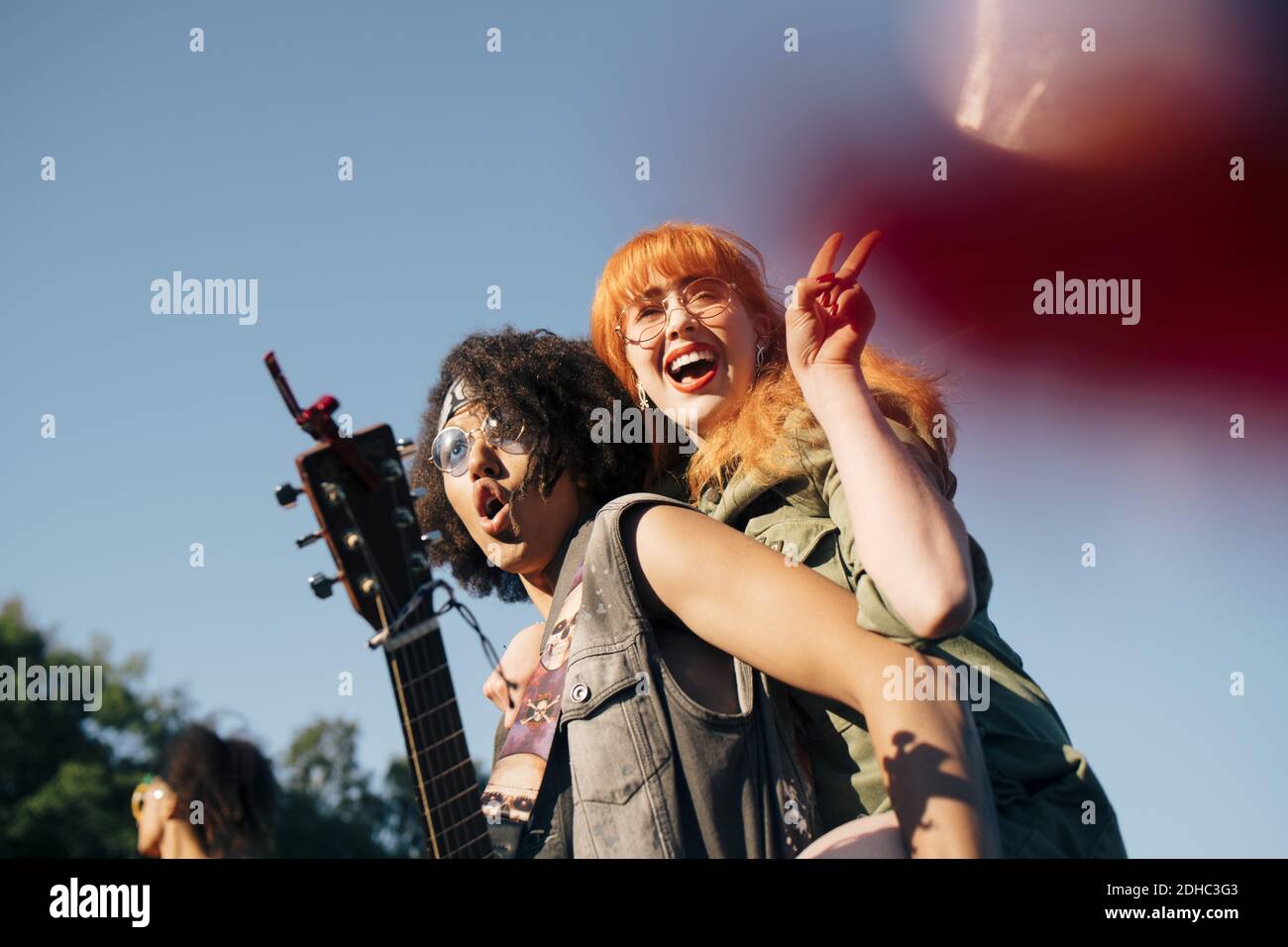 Uomo eccitato con ukulele piggybacking amico felice in caso contrario cielo Foto Stock