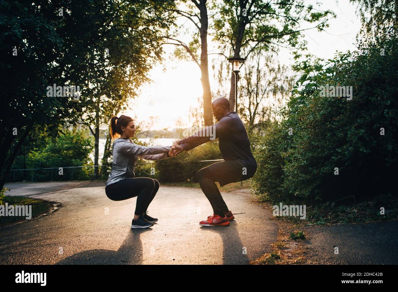 Atleti di sesso maschile e femminile che tengono le mani mentre praticano la posizione della sedia su strada nel parco Foto Stock