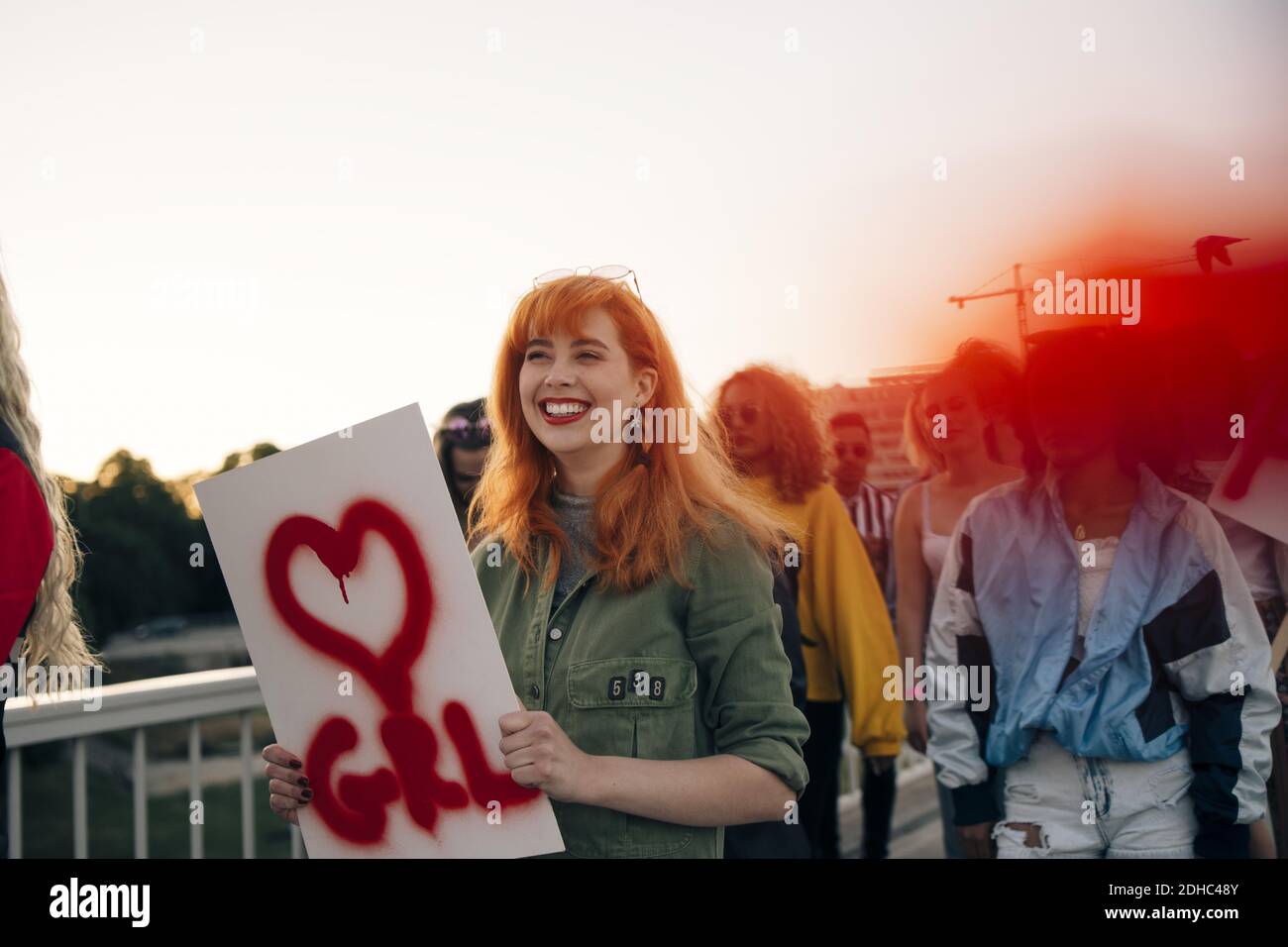 Donna sorridente con amici che marciano per i diritti delle donne in città contro il cielo Foto Stock