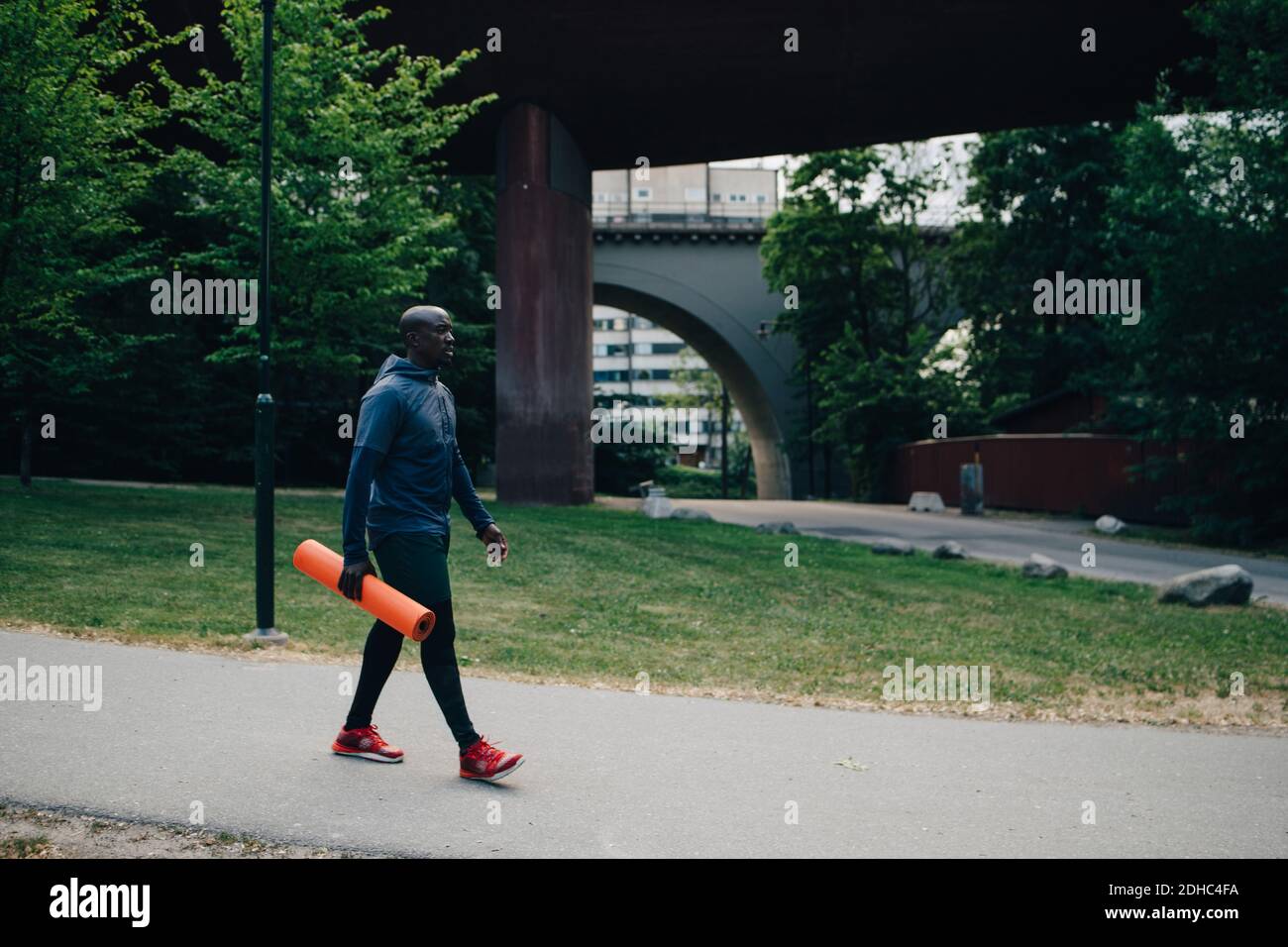 Un atleta maschile a lunghezza intera che tiene il tappetino yoga mentre cammina sul sentiero in città Foto Stock