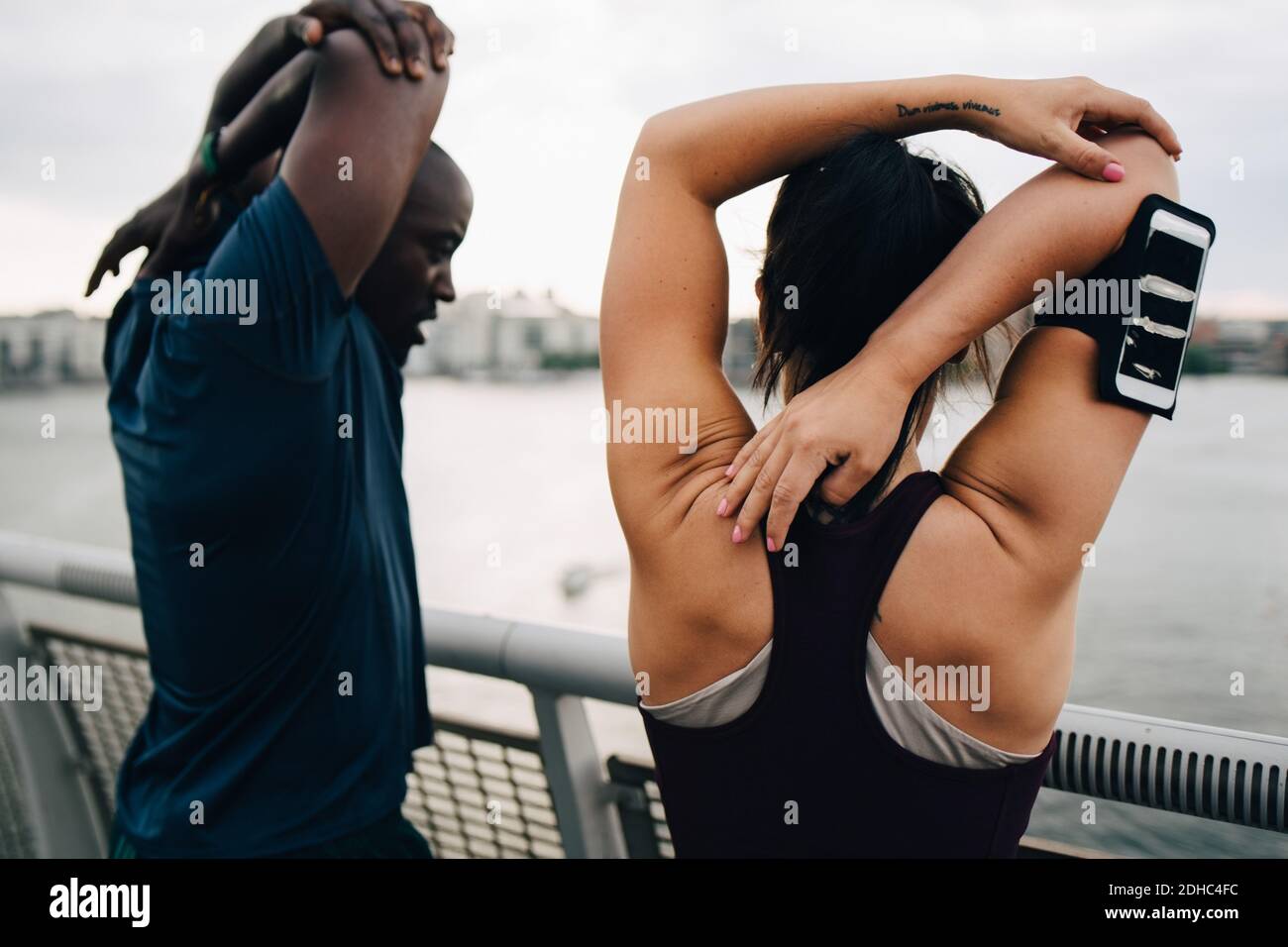 Atleti di sesso maschile e femminile che allungano le mani sul ponte pedonale sul mare in città Foto Stock