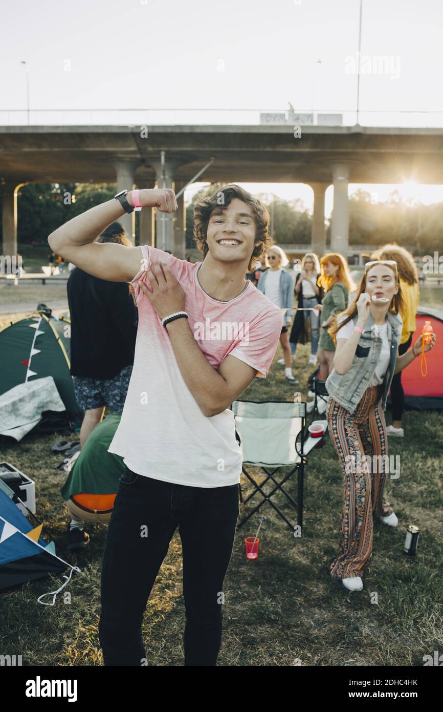Ritratto di un uomo sorridente che flette i muscoli mentre si divergono con gli amici in festival di musica Foto Stock