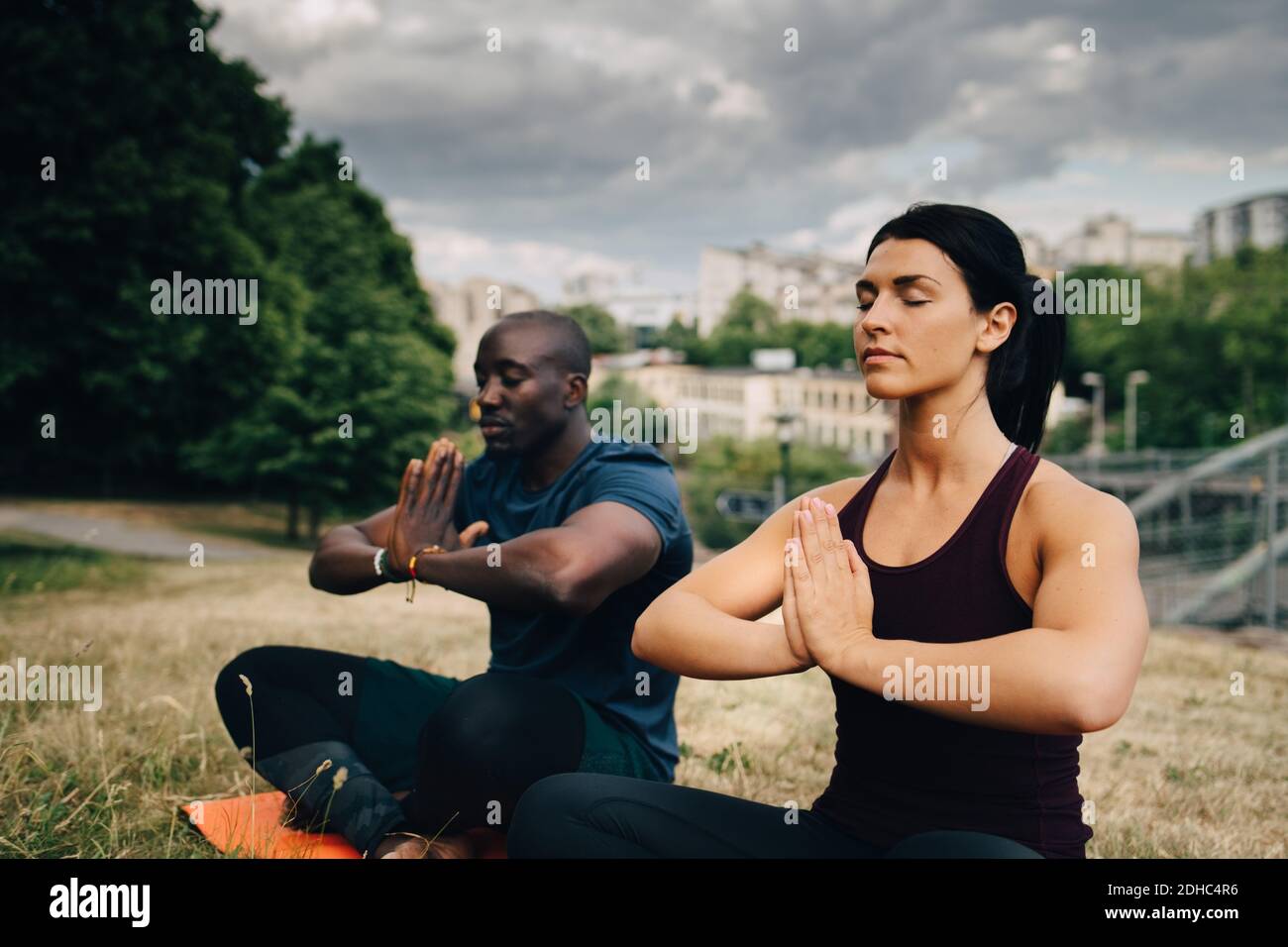 Amici multietnici che praticano lo yoga sul campo in città Foto Stock