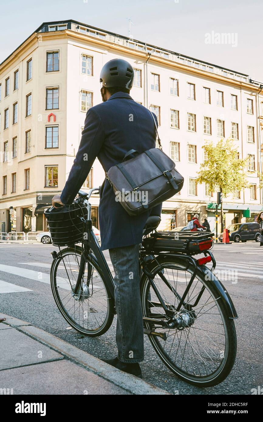 Vista posteriore del pendolari maschile in bicicletta elettrica sulla strada in città Foto Stock
