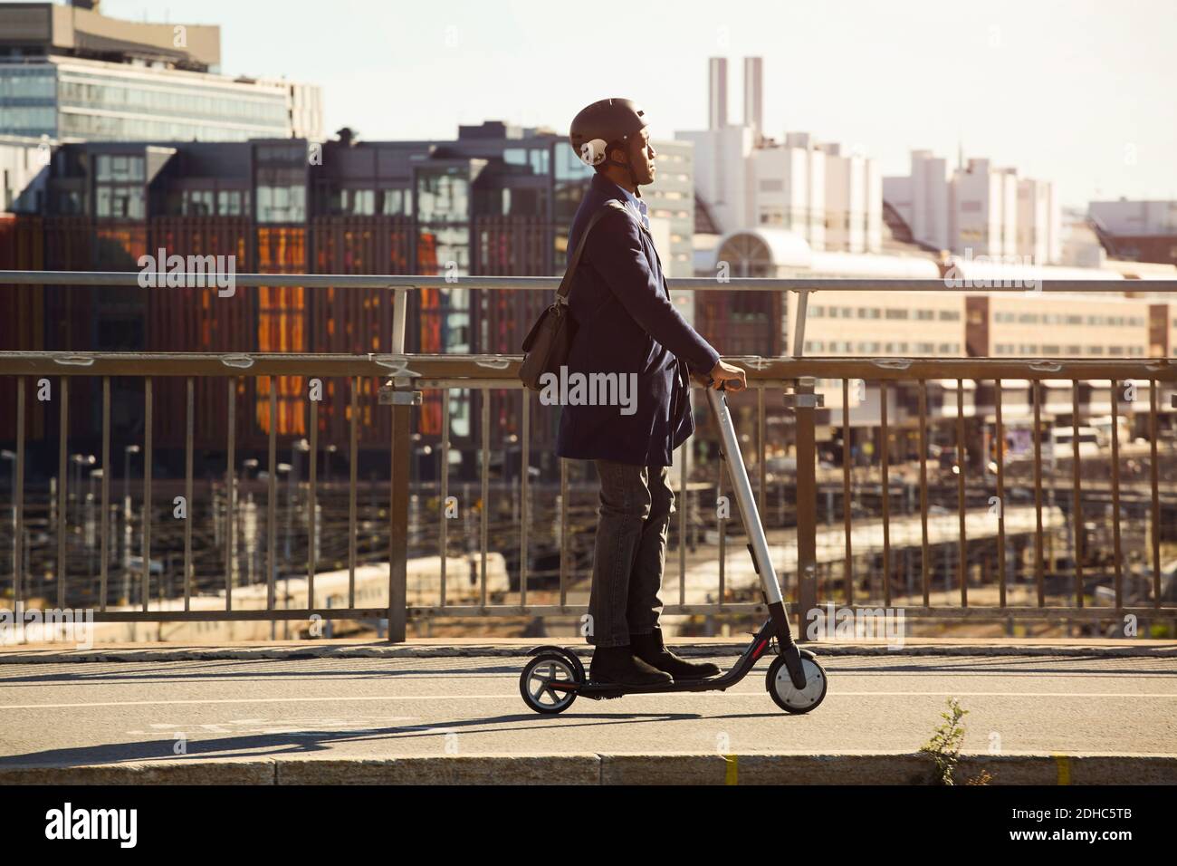 Vista laterale di un giovane uomo che guida uno scooter elettrico a spinta ponte in città Foto Stock