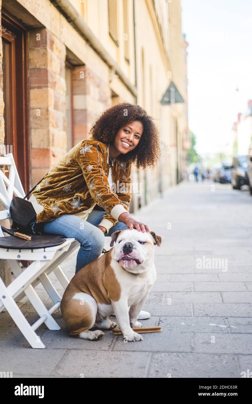 Donna sorridente seduta con il cane sul marciapiede in città Foto Stock