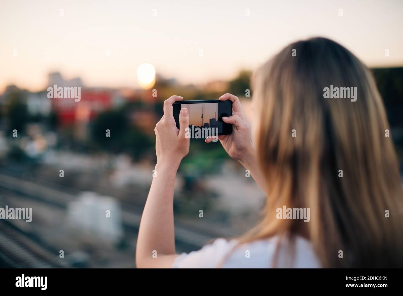 Giovane donna che fotografa Fernsehturm attraverso lo smartphone durante il tramonto Foto Stock
