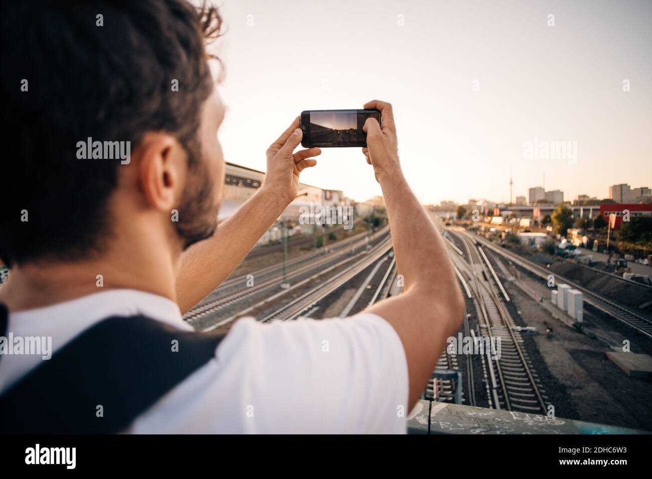 Giovane uomo che fotografa attraverso il telefono cellulare su binari ferroviari in città Foto Stock