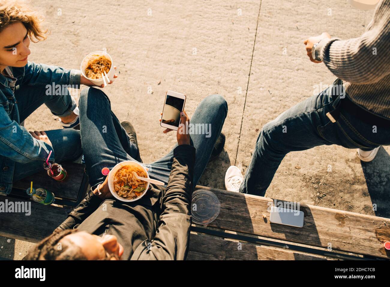 Vista ad alto angolo di un ragazzo adolescente che utilizza lo smartphone mentre mangiare con gli amici sulla strada in città Foto Stock