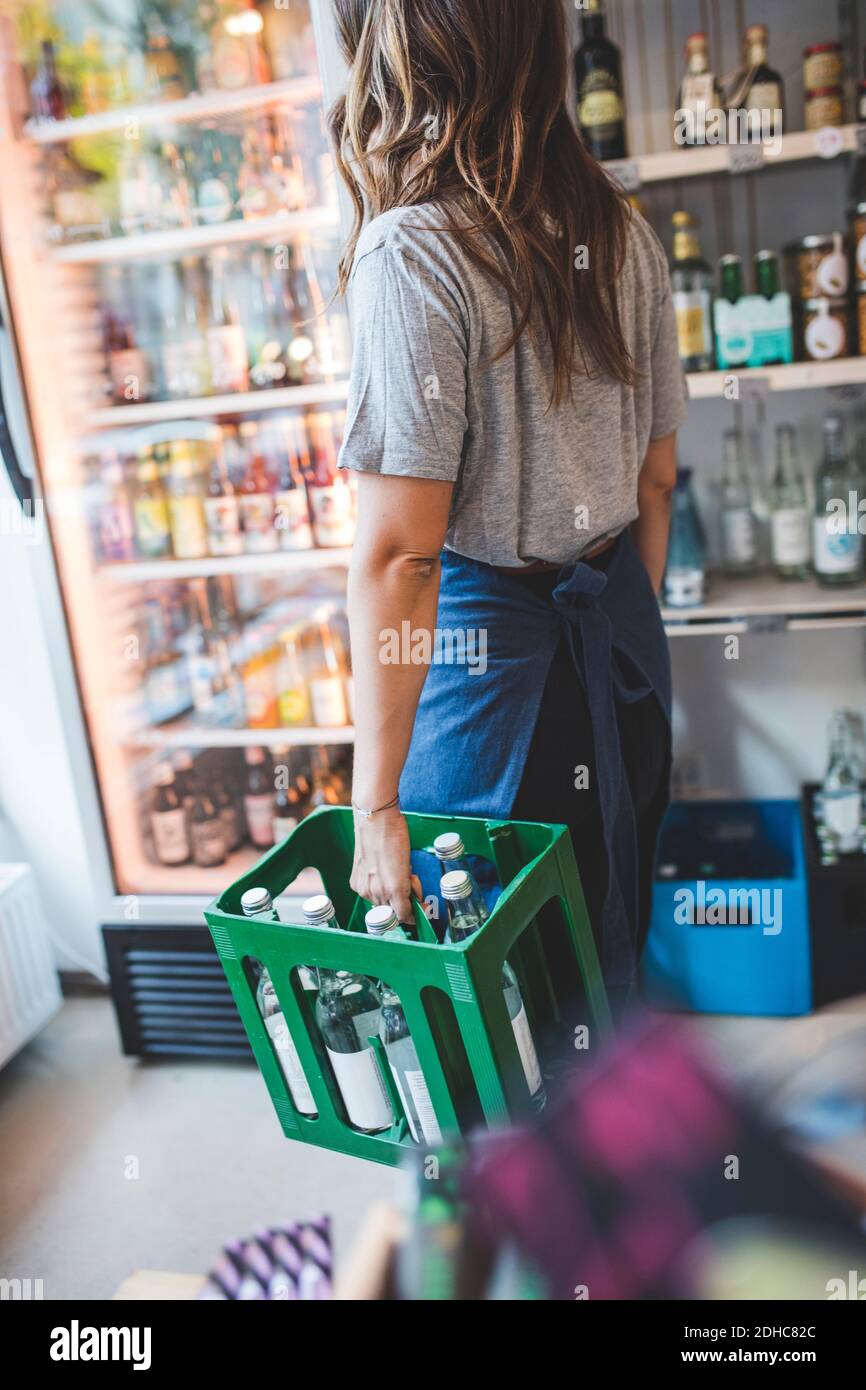 Dipendente femminile che trasporta bottiglie in cassa presso Deli Foto Stock