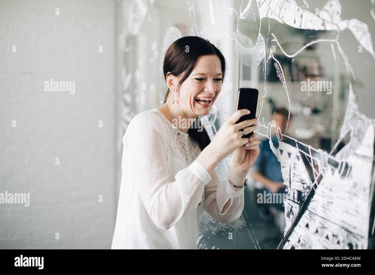 Donna d'affari creativa sorridente che prende selfie mentre si trova in piedi nella sala di bordo Foto Stock