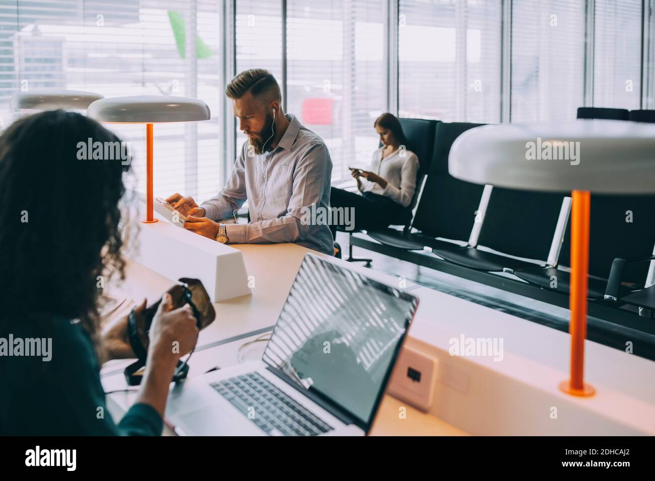 I colleghi che si occupano di lavoro utilizzano tecnologie mentre si siedono nell'area di partenza dell'aeroporto Foto Stock
