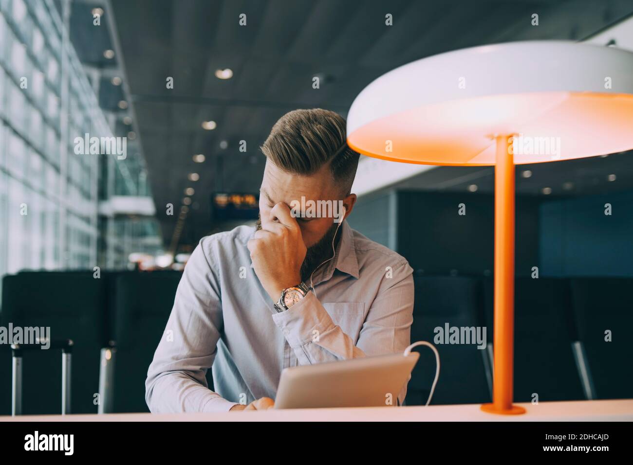 Uomo d'affari stanco seduto con il tablet digitale al tavolo mentre aspetta nella zona di partenza dell'aeroporto Foto Stock