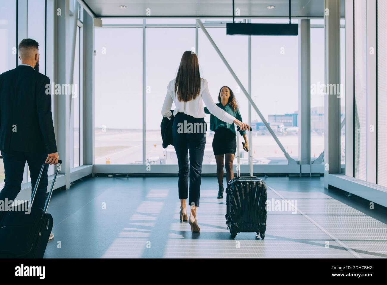 Donna d'affari sorridente che cammina verso una collega in corridoio all'aeroporto Foto Stock