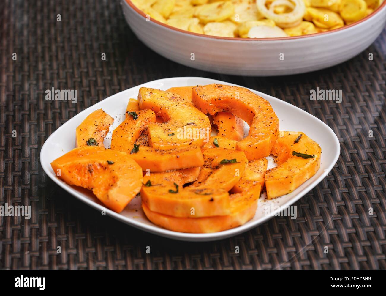 Pezzi di zucca d'arancia alla griglia con erbe, su piastra quadrata bianca,  un altro pieno di patate sullo sfondo Foto stock - Alamy