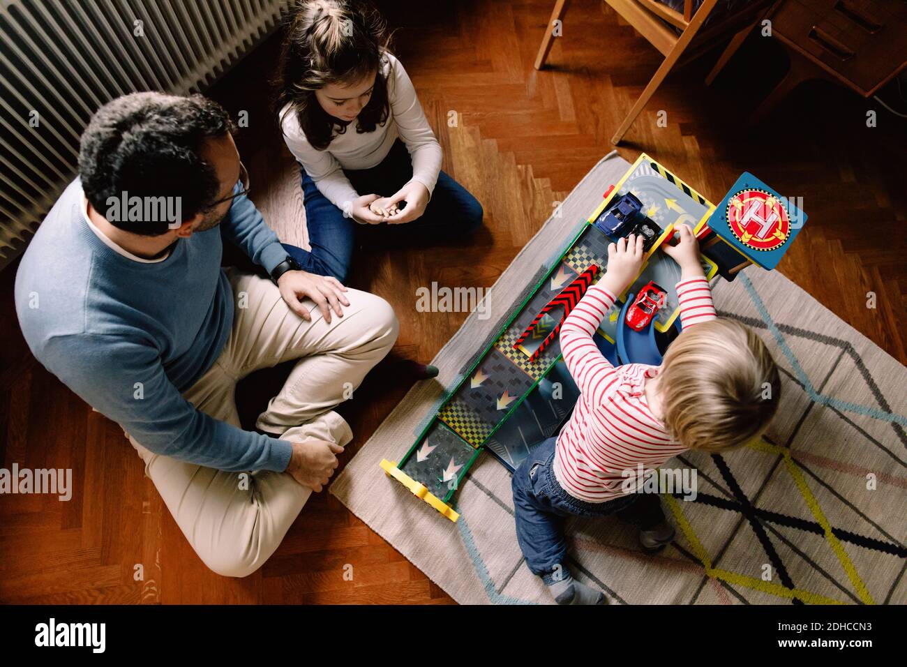 Vista ad alto angolo di padre e figlie con auto giocattolo a casa Foto Stock