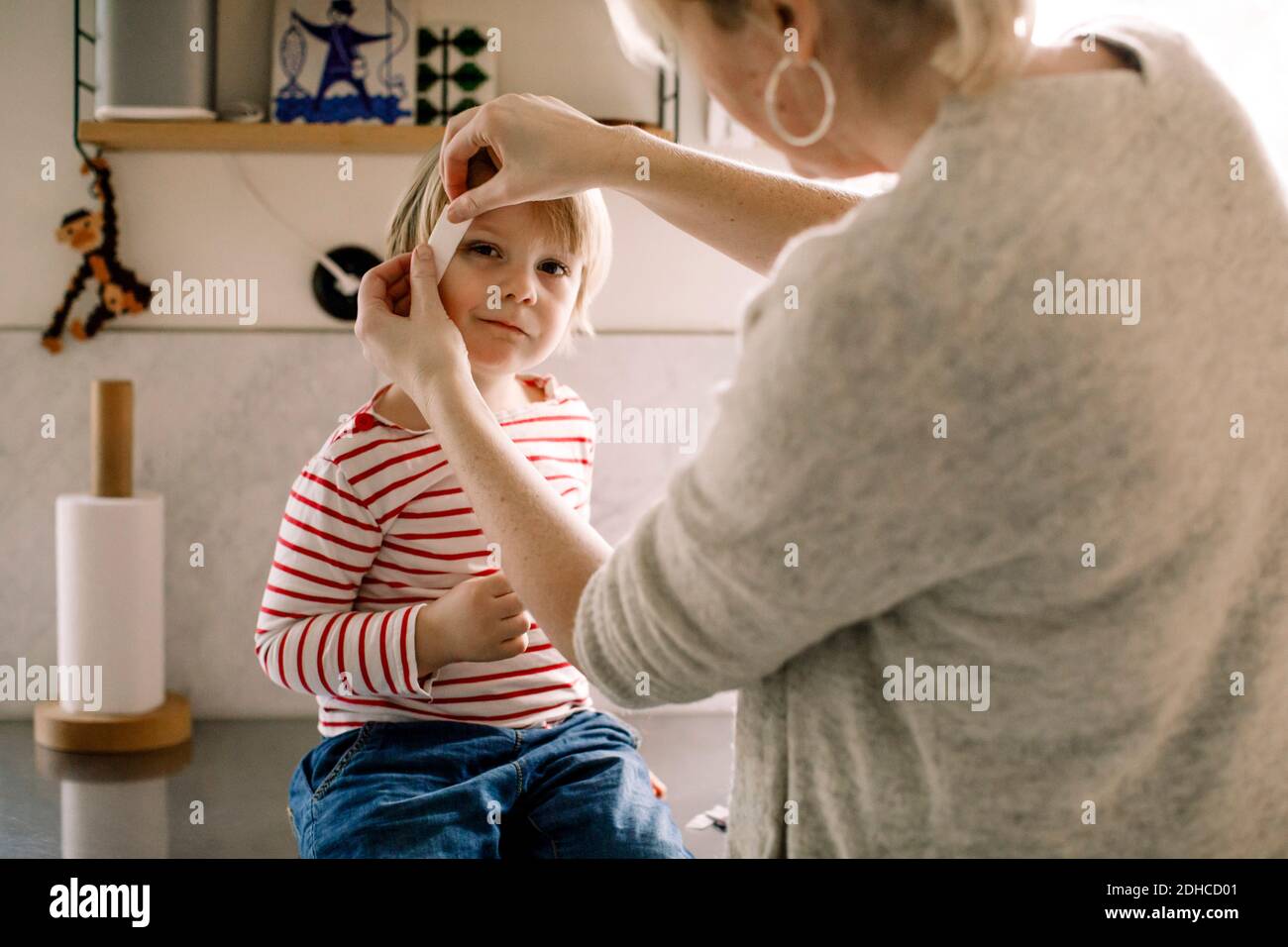 Madre che applica il bendaggio sulla faccia della figlia a casa Foto Stock