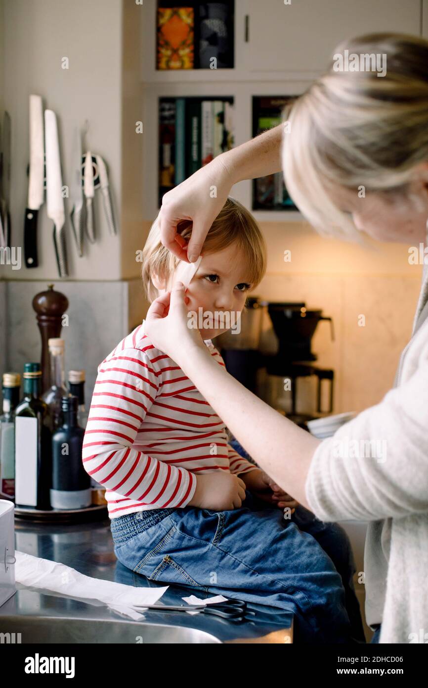Madre che applica il bendaggio sul viso della figlia in cucina a casa Foto Stock
