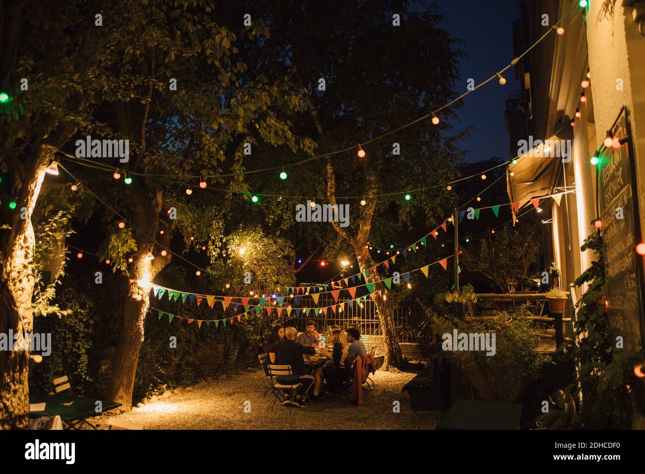 Amici multietnici che si divertano con una cena in cortile illuminato Foto Stock