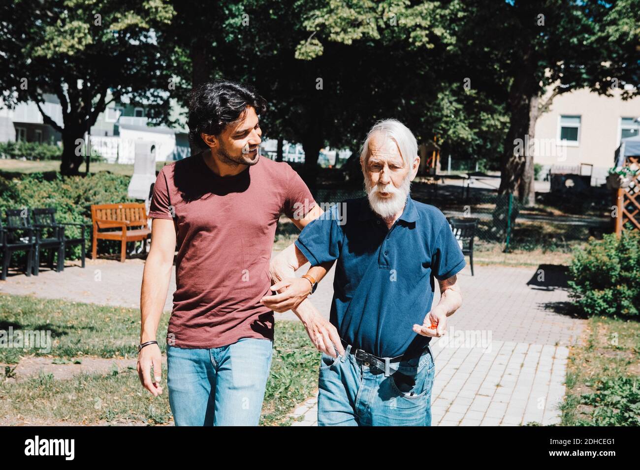 Sorridente uomo custode guardando mentre cammina braccio in braccio con uomo anziano a casa di cura Foto Stock