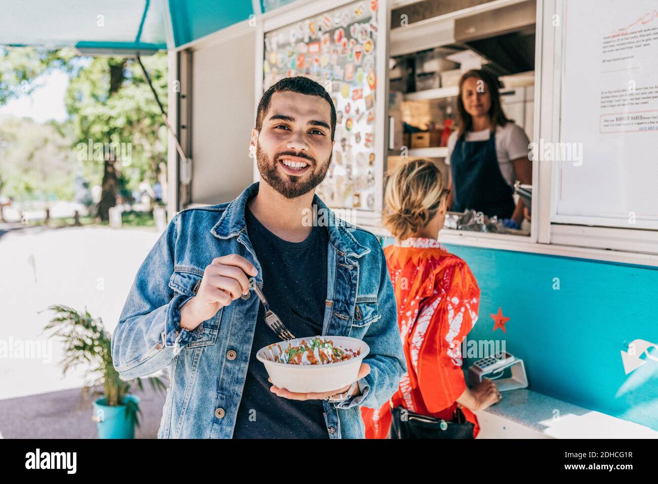 Ritratto di giovane sorridente che mangia fresco Tex-Mex in ciotola contro il camion del cibo Foto Stock