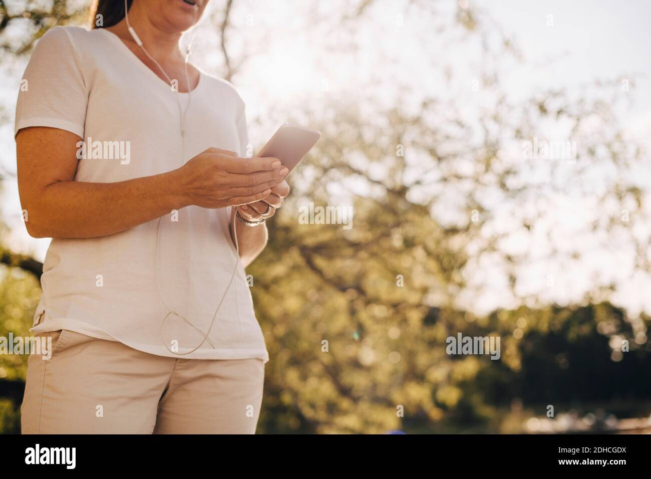 Sezione centrale ad angolo basso della donna che indossa le cuffie mentre il telefono cellulare in estate Foto Stock