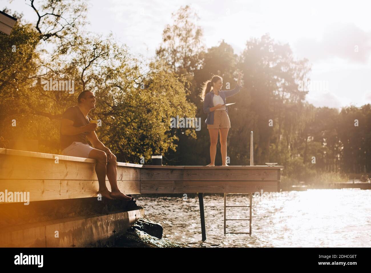 Sorridente coppia matura che parla mentre si guarda via patio vicino lago durante il giorno di sole Foto Stock