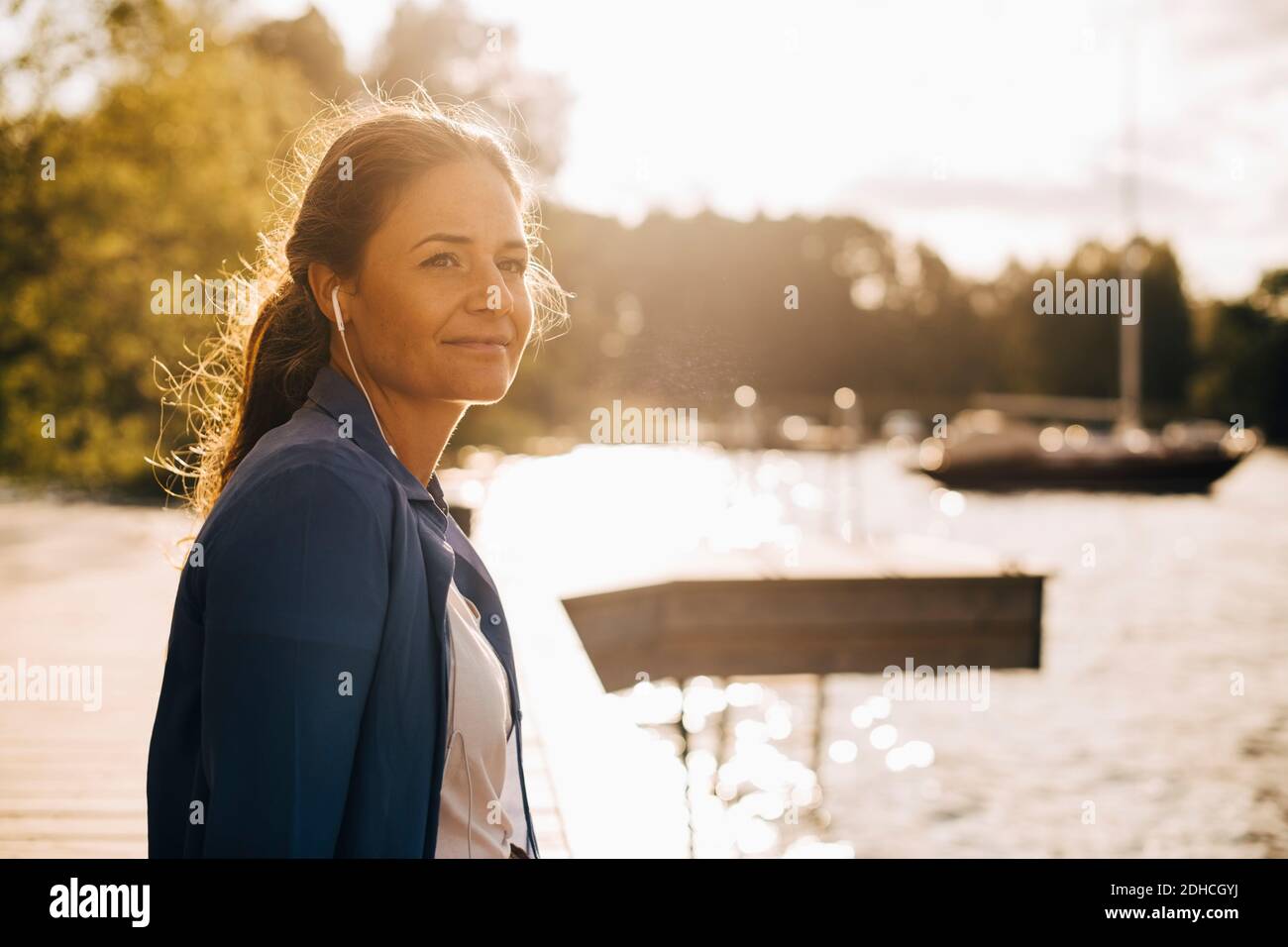 Donna premurosa che ascolta la musica con le cuffie mentre si siede sul lago in vacanza estiva Foto Stock