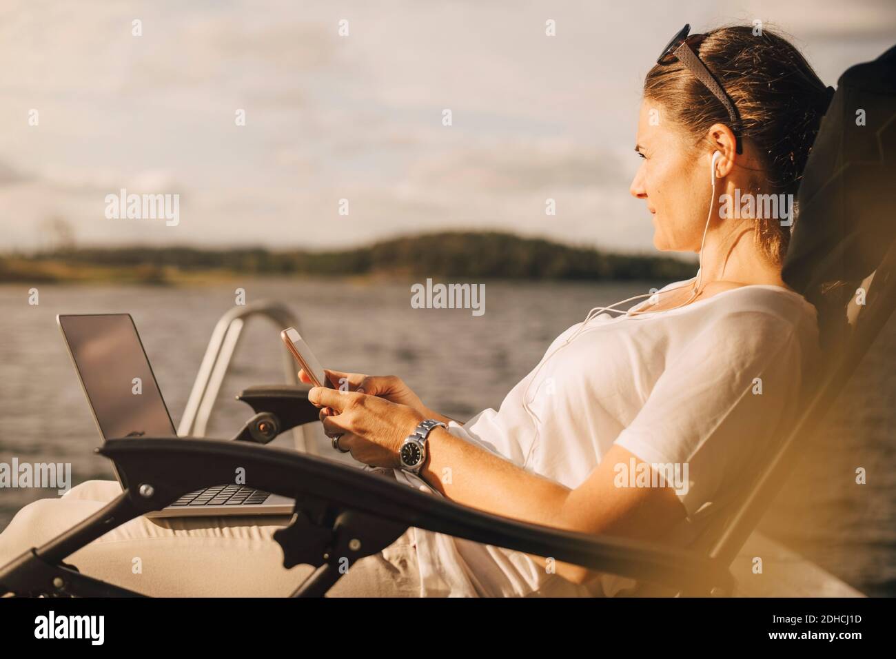 Donna premurosa con computer portatile che usa il telefono cellulare contro il lago Foto Stock