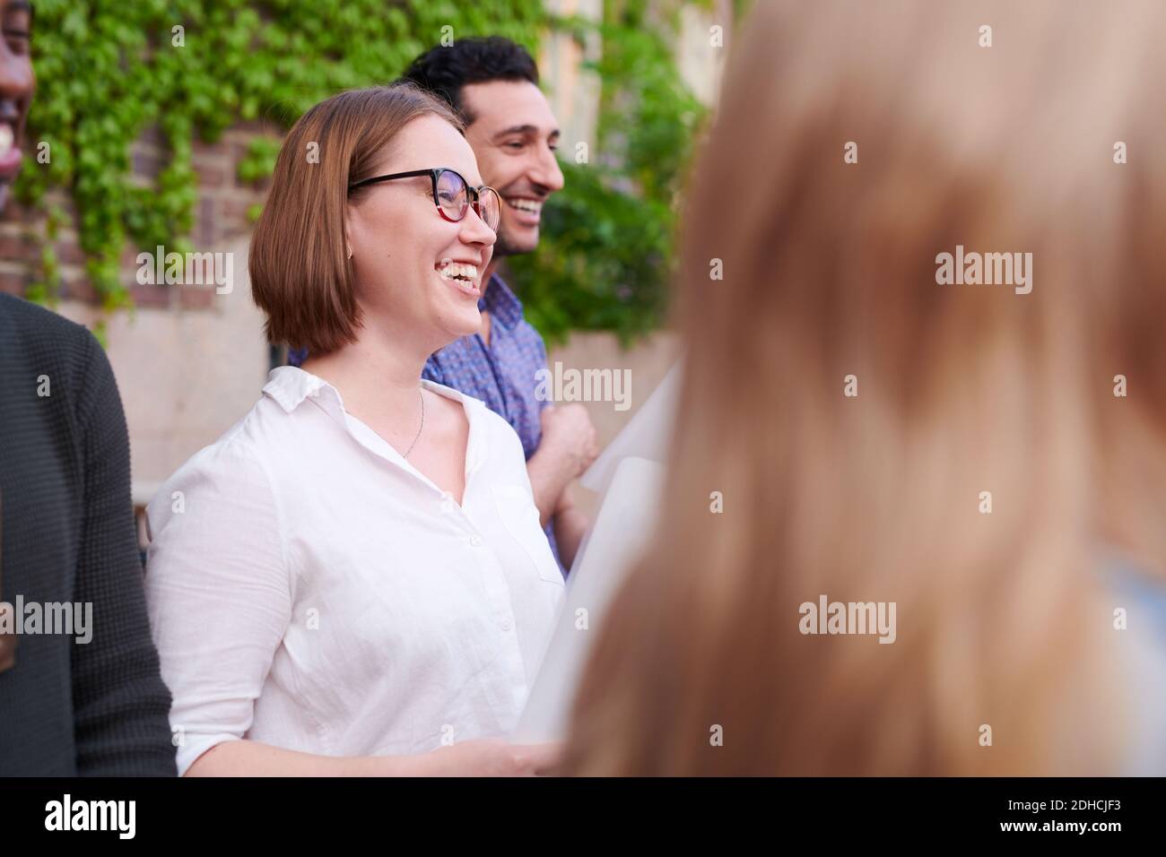 Giovane donna sorridente con amici che cantano in coro al di fuori della lingua scuola Foto Stock